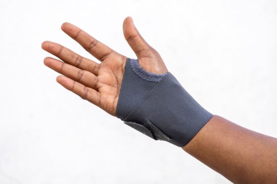 Hand wearing a dark wrist support or brace against a plain background