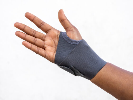 Hand wearing a grey wrist support brace against white background