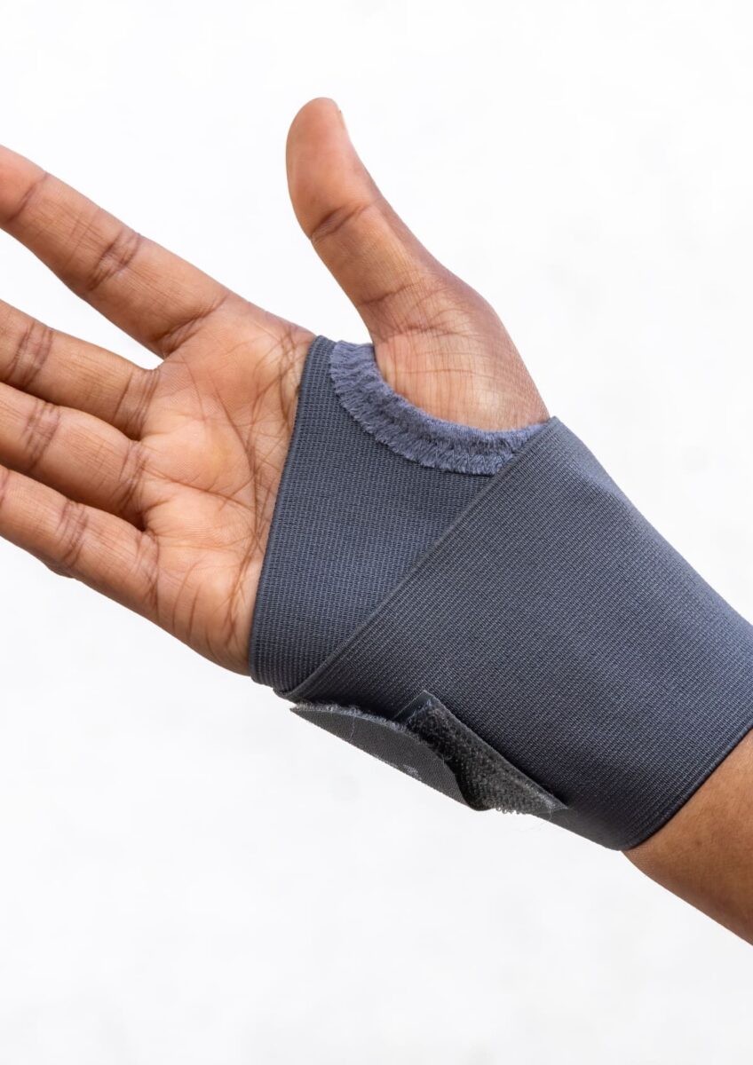 Hand wearing a grey wrist support brace against white background