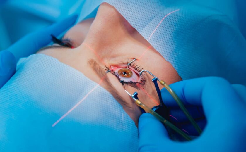 Patient undergoing eye surgery with eyelid held open and laser targeting eye