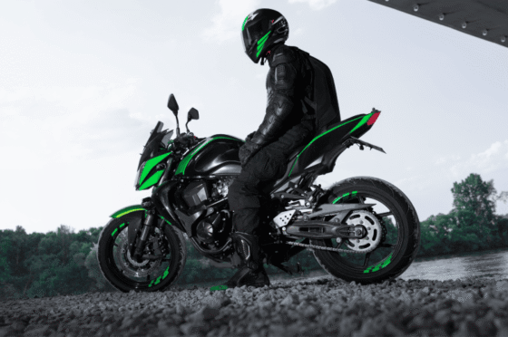 Motorcyclist in black gear and helmet sitting on a black and green motorcycle near a river under a structure