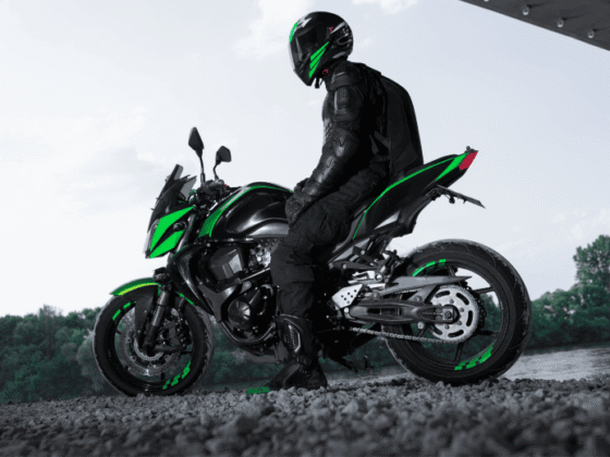 Motorcyclist in black gear and helmet sitting on a black and green motorcycle near a river under a structure