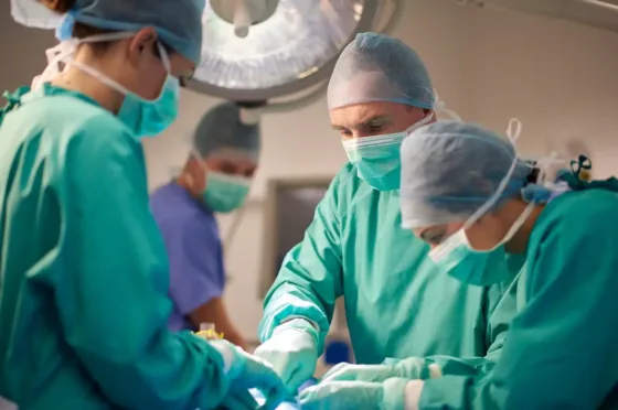 Surgical team dressed in scrubs and masks performing operation in operating theatre