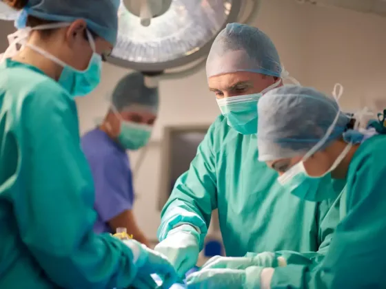 Surgical team dressed in scrubs and masks performing operation in operating theatre