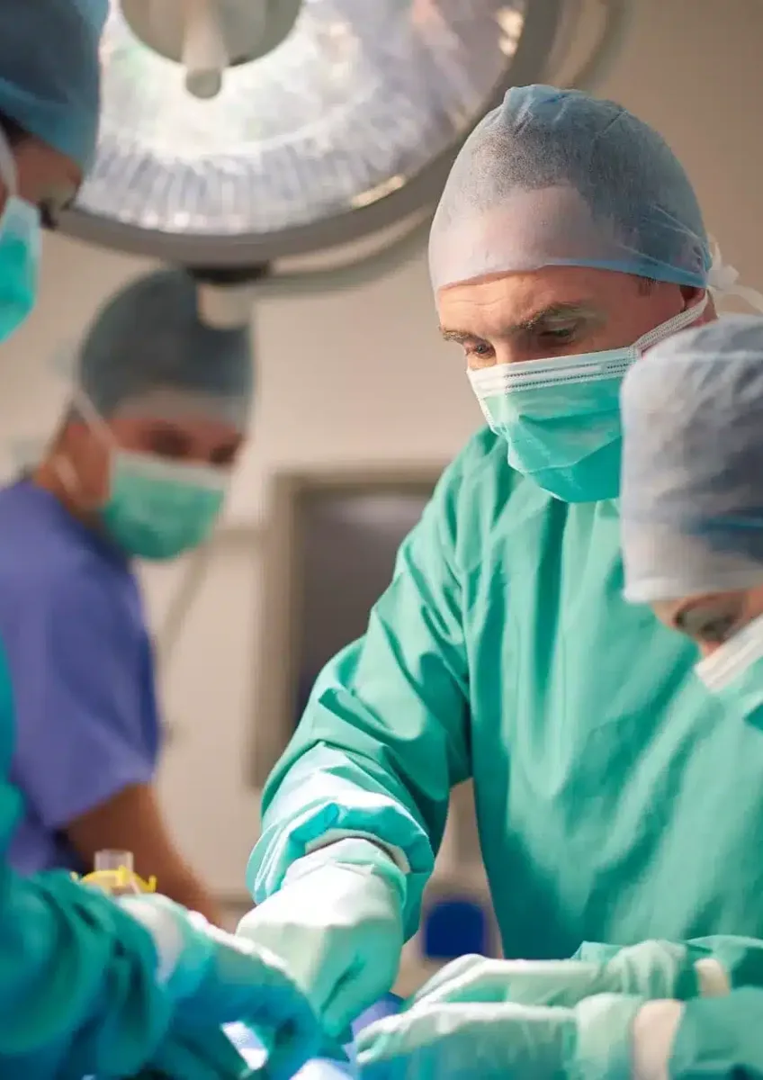 Surgical team dressed in scrubs and masks performing operation in operating theatre