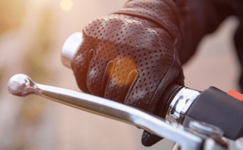 Gloved hand gripping motorcycle handlebar and brake lever in sunlight
