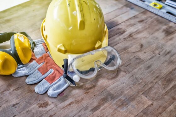 Yellow hard hat, gloves, ear protectors, and safety goggles on wooden table