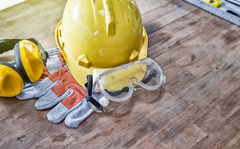 Yellow hard hat, gloves, ear protectors, and safety goggles on wooden table