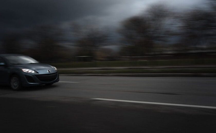 Dark car driving quickly on a road with blurred motion effect