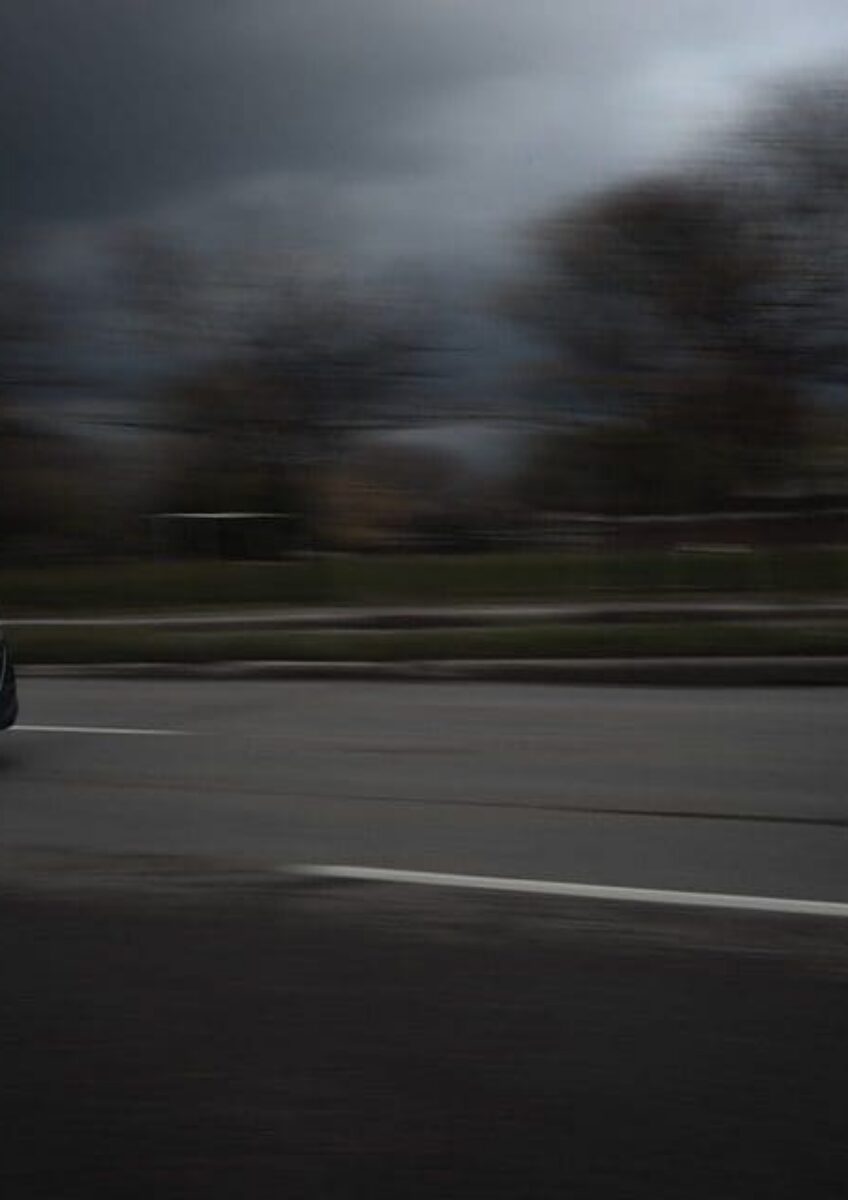 Dark car driving quickly on a road with blurred motion effect