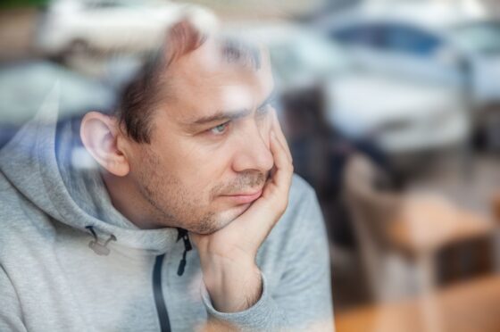 Man leaning head on hand, looking pensively through a window in a café