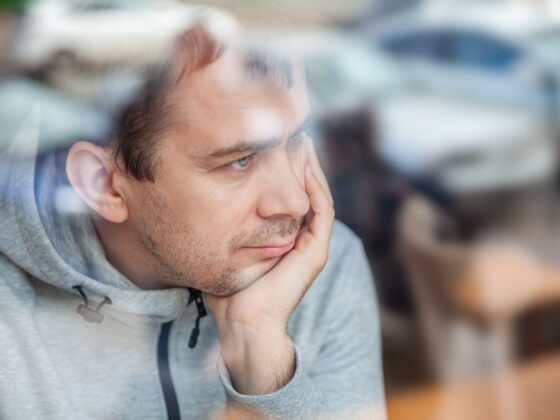 Man leaning head on hand, looking pensively through a window in a café