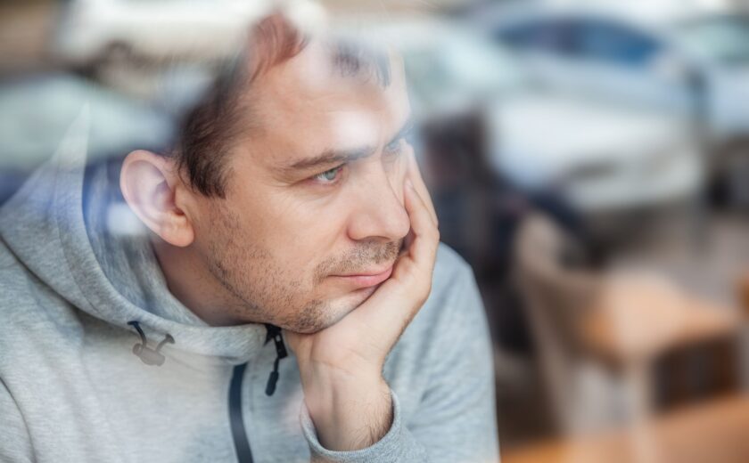 Man leaning head on hand, looking pensively through a window in a café