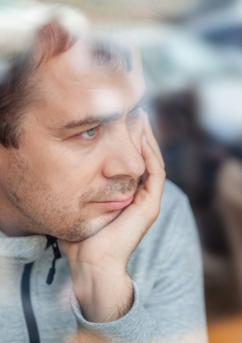 Man leaning head on hand, looking pensively through a window in a café