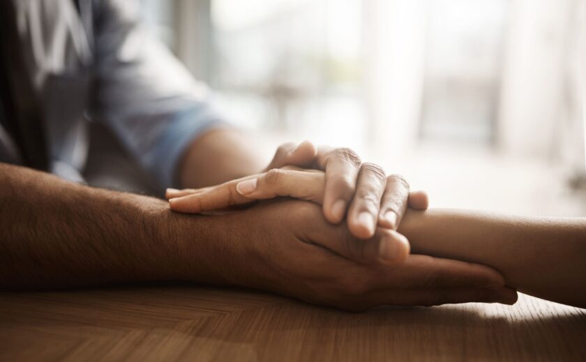 Two people holding hands on a wooden table in soft light