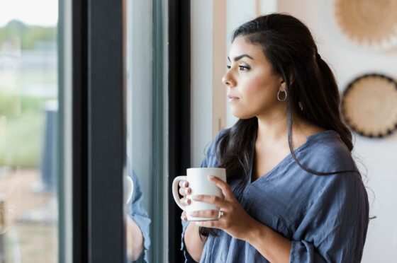 Mid adult woman stands at window with hot drink