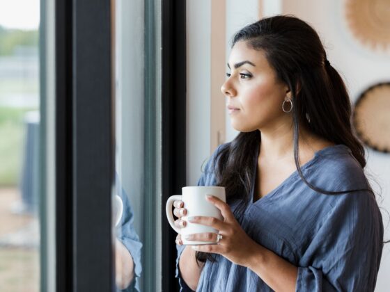 Mid adult woman stands at window with hot drink