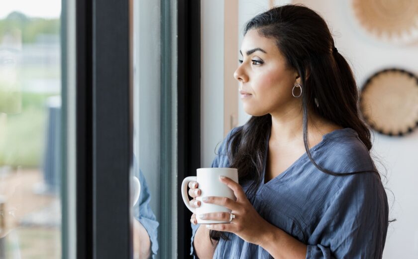Mid adult woman stands at window with hot drink