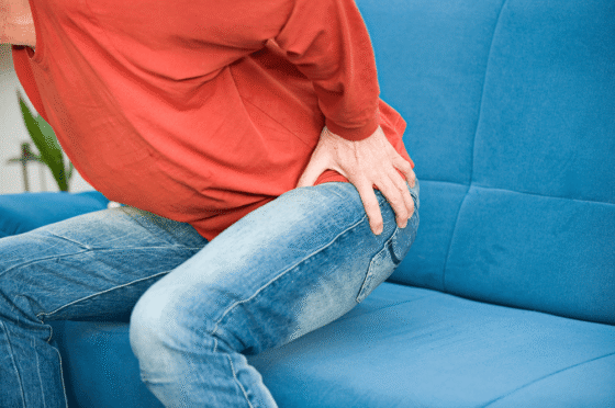 Person in red top and jeans sitting, holding hip in apparent pain