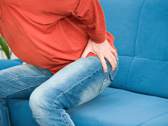 Person in red top and jeans sitting, holding hip in apparent pain