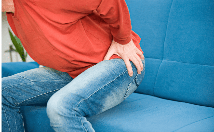 Person in red top and jeans sitting, holding hip in apparent pain