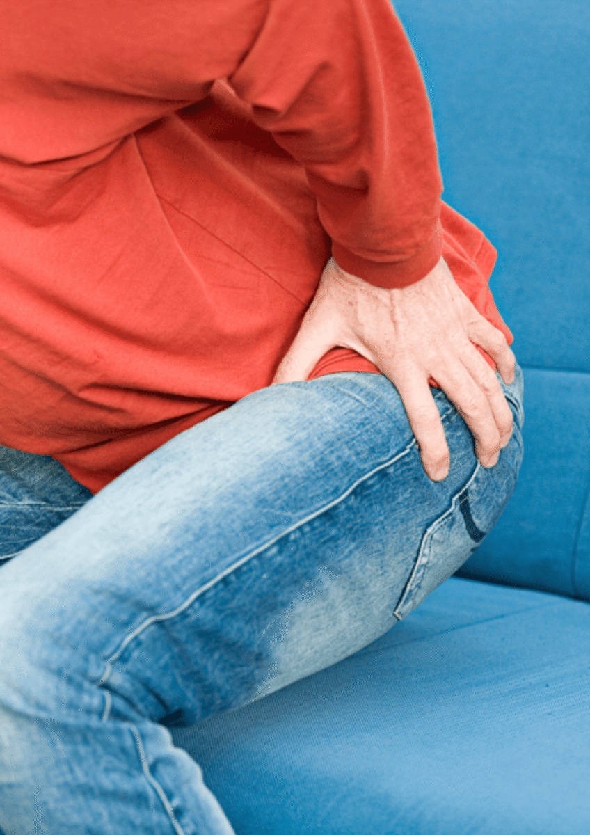 Person in red top and jeans sitting, holding hip in apparent pain