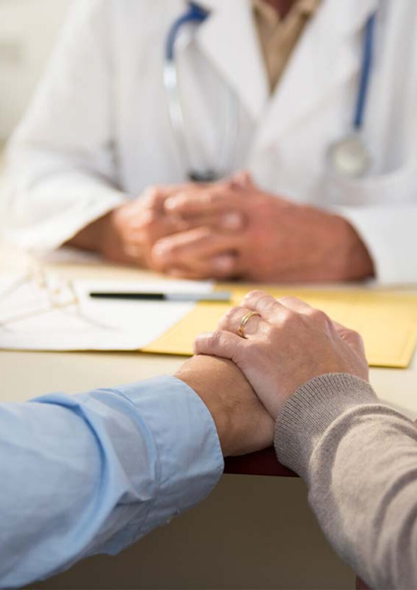 Two people holding hands in consultation with doctor at desk