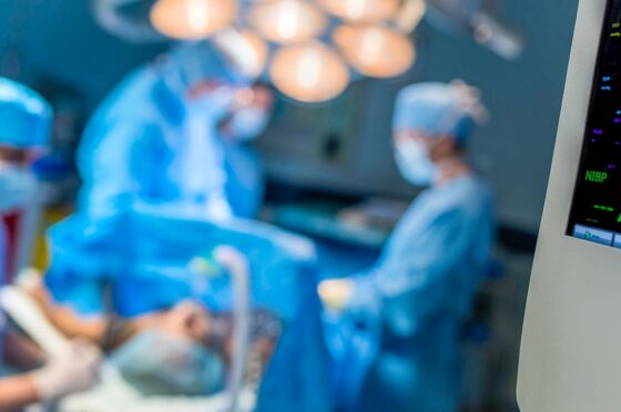 Blurred surgical team operating in brightly lit operating theatre with medical monitor in foreground