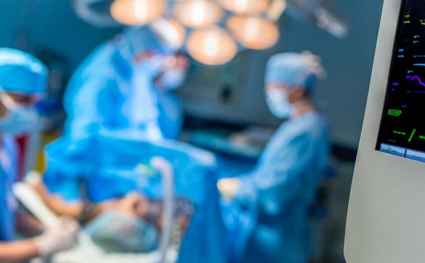 Blurred surgical team operating in brightly lit operating theatre with medical monitor in foreground