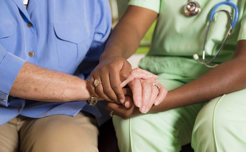 Medical professional holding hands with an elderly person for comfort