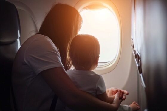 Woman holding a toddler looking out an airplane window with sunlight