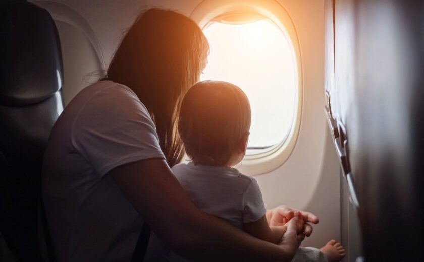 Woman holding a toddler looking out an airplane window with sunlight