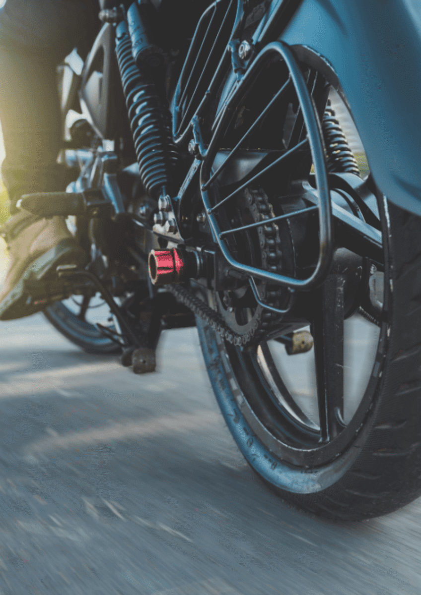 Close-up of motorcycle rear wheel and chain with rider on road