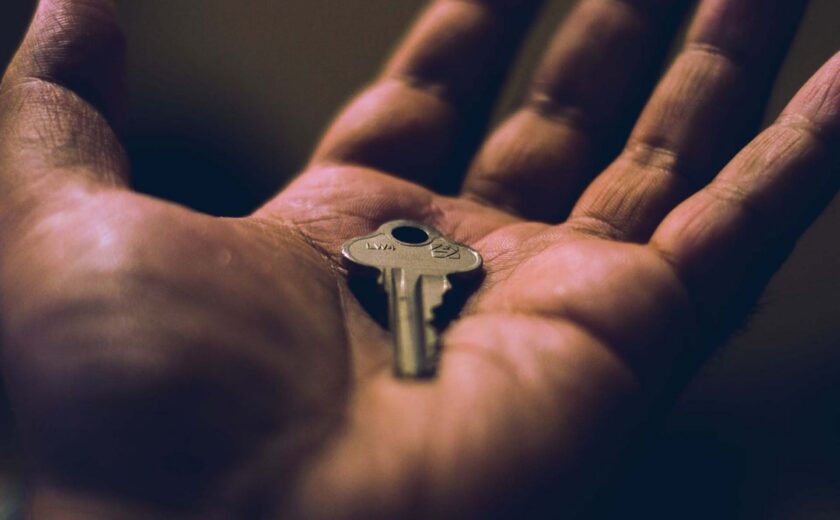 Close-up of hand holding small silver key on palm with dark background
