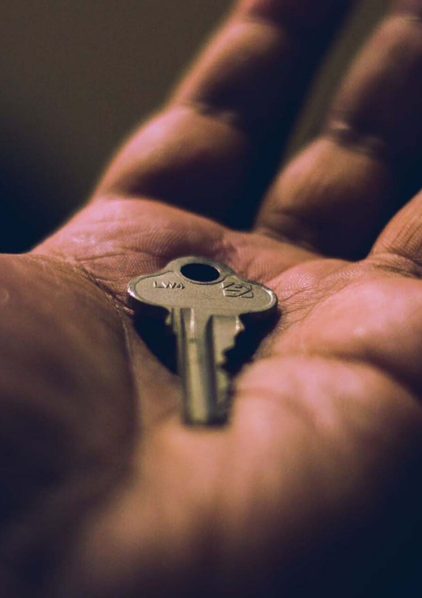 Close-up of hand holding small silver key on palm with dark background