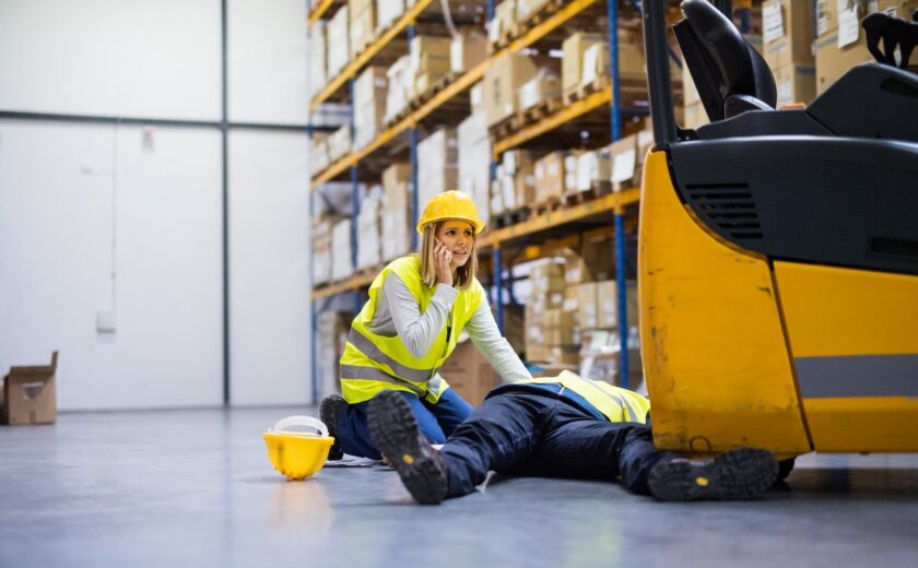 Female worker calling for help beside a male worker lying injured in warehouse